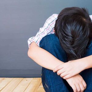 A young boy sitting with his head between his legs